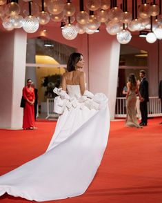 a woman in a white dress is walking down the red carpet with balloons hanging from the ceiling