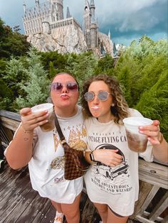 two people standing next to each other in front of hogwarts castle holding drinks