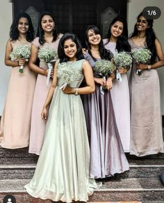 a group of women standing next to each other in dresses and holding bouquets on steps