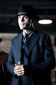 a man in a suit and hat standing with his hands folded