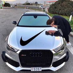 a man leaning over the hood of a silver car with a nike logo on it