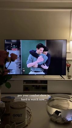 a flat screen tv sitting on top of a white table next to a vase with flowers