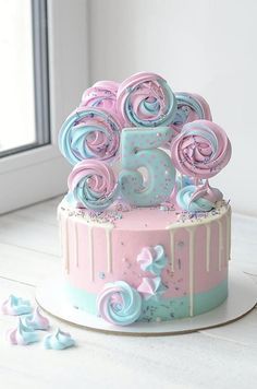 a pink and blue cake sitting on top of a white table next to a window