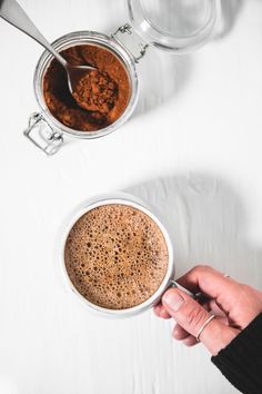 a person holding a cup of hot chocolate in their left hand, with another mug on the right