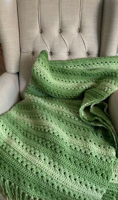 a green crocheted blanket sitting on top of a chair next to a pillow