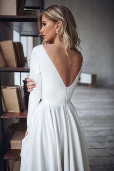 a woman standing in front of a bookshelf wearing a white dress with open back