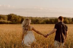 a man and woman holding hands while walking through a wheat field in the evening sun