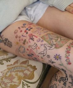 a woman with tattoos on her arm and leg sitting next to a pillow covered in flowers