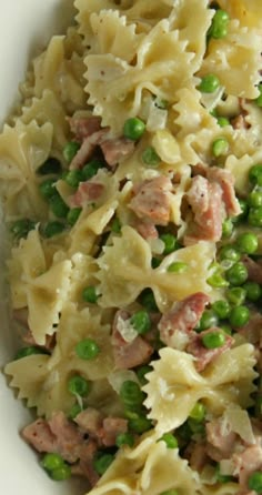 a white bowl filled with pasta, peas and ham on top of a wooden table