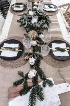 the table is set with black and white plates, silverware, greenery and gold candlesticks