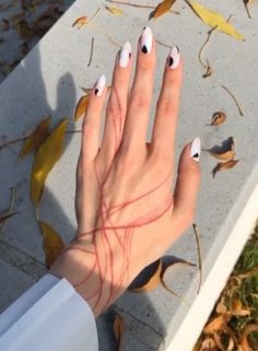 a woman's hand with white and black nail polish on it sitting next to leaves