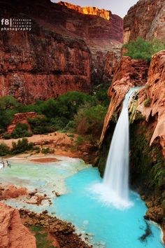 a waterfall in the middle of a canyon with blue water running down it's sides