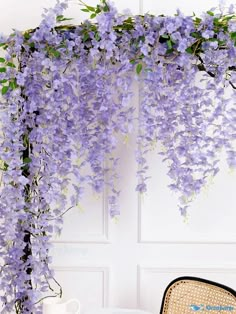 wistery purple flowers hang from the side of a white wall next to a chair