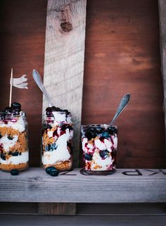 three jars filled with dessert sitting on top of a wooden shelf next to each other