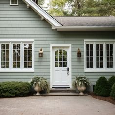 a gray house with white windows and two large planters on the front door area