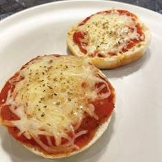 two small pizzas sitting on top of a white plate covered in cheese and sauce