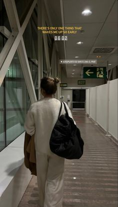 a woman walking down a hallway carrying a black handbag in her right hand and an exit sign on the wall behind her