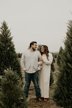 a man and woman standing next to each other in a field full of christmas trees