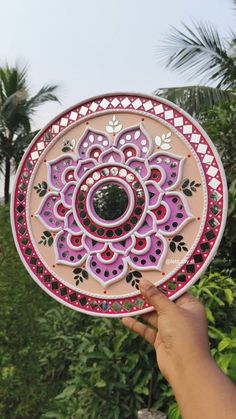 a hand holding up a decorative plate in front of some trees