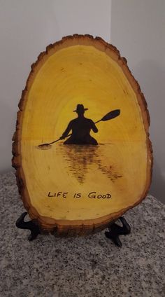 a wooden plaque with a man in a kayak on the water that says life is good