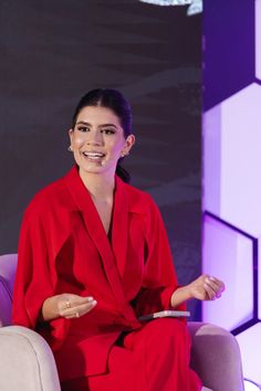 a woman in a red suit sitting on a chair with her hands out to the side