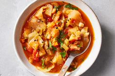 a white bowl filled with vegetable soup on top of a gray counter next to a spoon