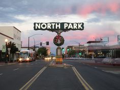 a city street with cars and buses driving down the road at dusk, near a sign that says north park