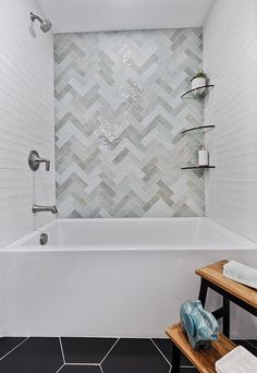 a bathroom with a white tub and black floor tiles on the walls, along with a wooden bench