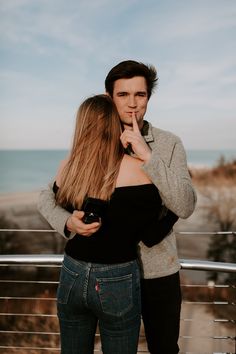 a man and woman standing next to each other near the ocean with their hands on their lips