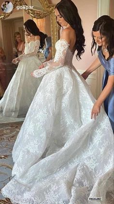 a woman in a wedding dress looking at her reflection in the mirror while another woman stands nearby