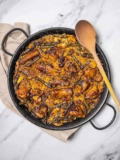 an iron skillet filled with food on top of a white counter next to a wooden spoon