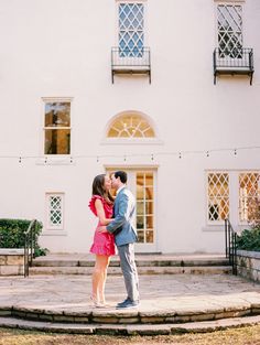 a man and woman kissing in front of a white building with steps leading up to it