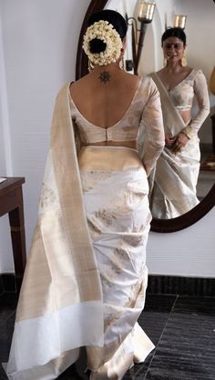 a woman standing in front of a mirror wearing a white sari with flowers on it