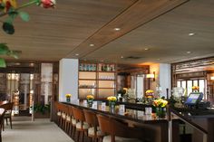 a long bar with lots of chairs and flowers on the counter top in front of it