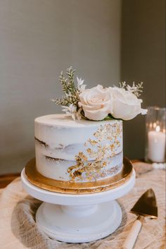 a white and gold wedding cake with flowers on the top is sitting on a table