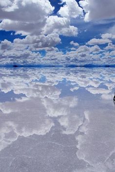 a large body of water with clouds in the sky and one boat on it's side