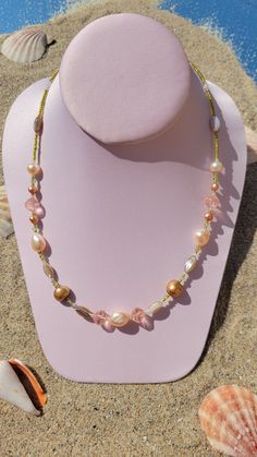 A beautiful necklace laying upon sand and shells as if it were on a sunny beach. The necklace is handmade by brand Gypsy Caravan Design and includes colored fresh water pearls, peach colored Czech glass beads and delicate green seed beads to resemble sunlit seaweed from under the sea. Multicolor Bohemian Jewelry With Pearl Drop, Bohemian Multicolor Pearl Drop Jewelry, Gold Bohemian Single Strand Pearl Necklace, Bohemian Pearl Shell Necklace With Round Beads, Bohemian Single Strand Pearl Jewelry, Pink Bohemian Beaded Shell Necklace, Pink Beaded Bohemian Shell Necklace, Bohemian Single Strand Pearl Necklace For Beach, Festival Pearl Jewelry With Colorful Beads