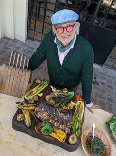 an older woman standing next to a tray of food on a table with other foods