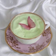 a pink and gold plate holding a cup with green liquid in it on a white cloth