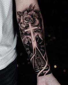 a man with a cross and roses tattoo on his arm is holding a clock in front of him