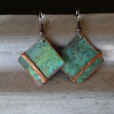 two square shaped earrings with copper and green patters on them, hanging from silver hooks