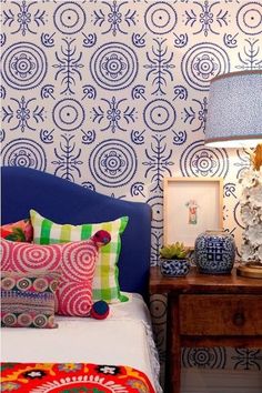 a bedroom with blue and white wallpaper and colorful pillows on the bed in front of it