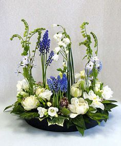 an arrangement of white and blue flowers in a black bowl on top of a table