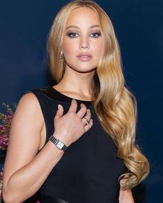 a woman with long blonde hair wearing a black dress and holding her hand up to her chest