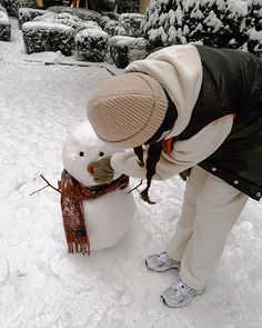 a woman building a snowman outside in the snow