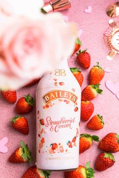 a bottle of bailey's strawberry cream next to strawberries on a pink background