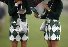 two women in green and white skirts hold umbrellas over their heads as they stand on the field