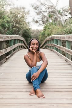 a woman is sitting on a bridge talking on her cell phone and smiling at the camera