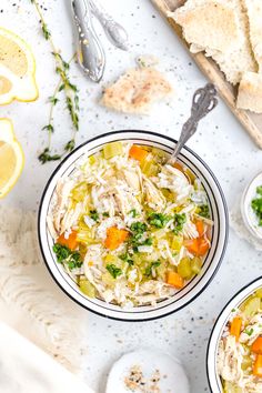 two bowls filled with soup next to sliced lemons and bread on a white surface