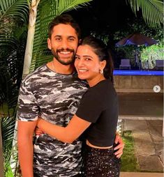 a man and woman standing next to each other in front of a pool at night